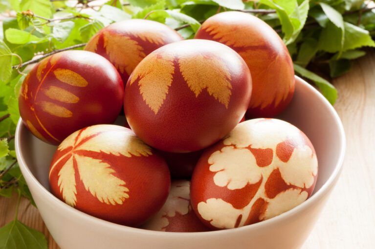easter eggs dyed with onion peels, with a pattern of fresh herbs, in a white bowl